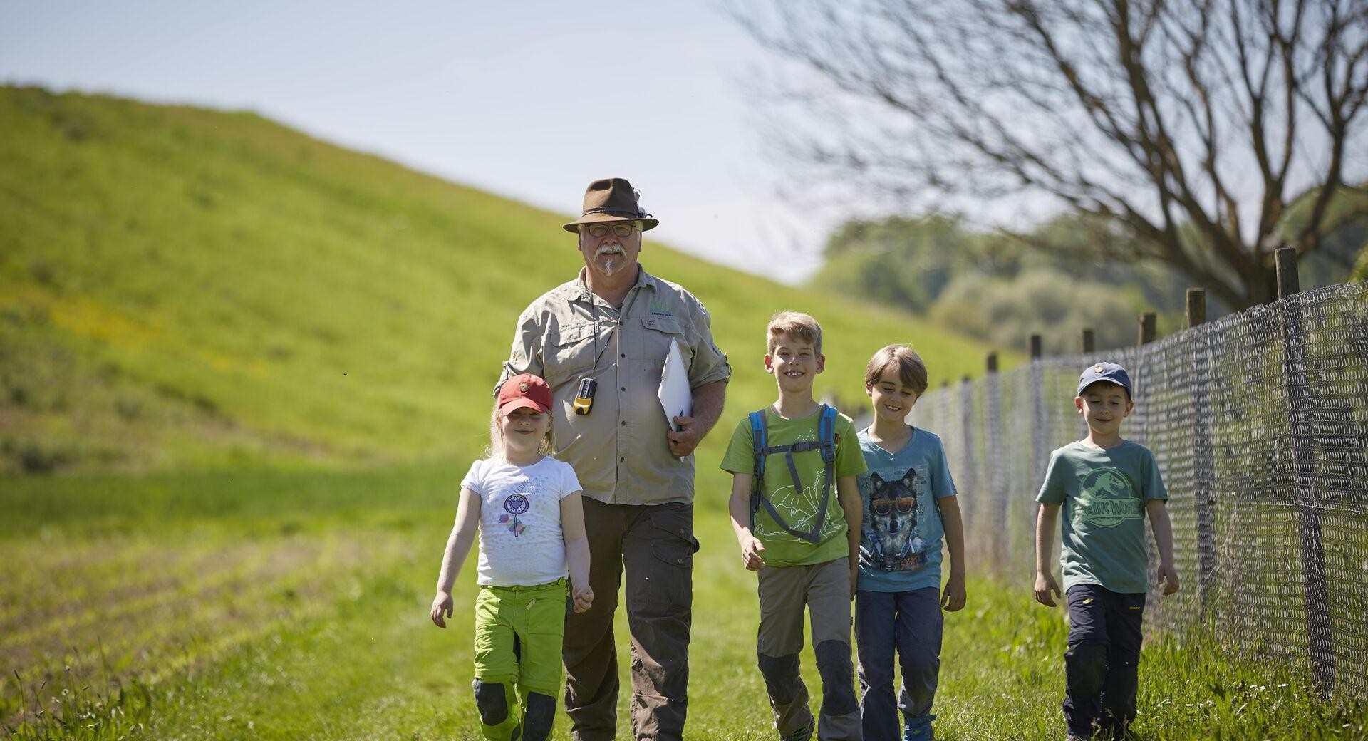 Kinder entdecken mit einem Ranger ihre Umwelt Vier Kinder laufen mit einem Ranger über eine grüne Wiese