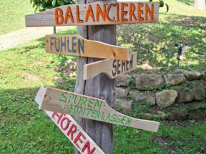 Vogelhäuschen im Grünen, an welchem verschiedene Holzschilder mit bunten Aufschriften angebracht sind.