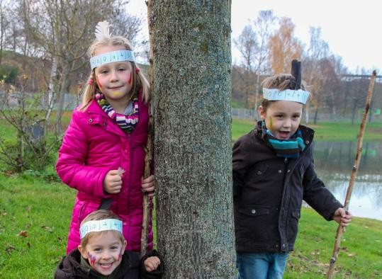 Drei Kinder, verkleidet als Indianer, stehen um einen Baum herum