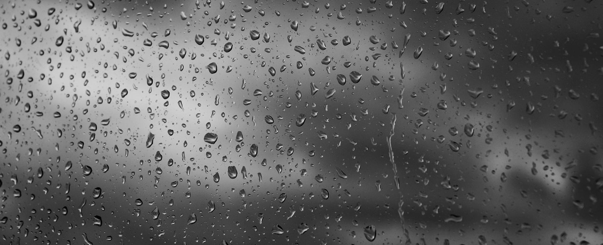 Regentropfen an Scheibe vor grauem Unwetterhimmel