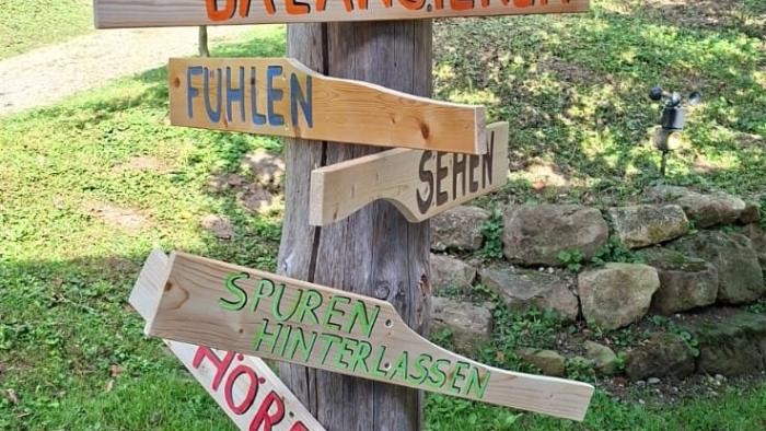 Vogelhäuschen im Grünen, an welchem verschiedene Holzschilder mit bunten Aufschriften angebracht sind.