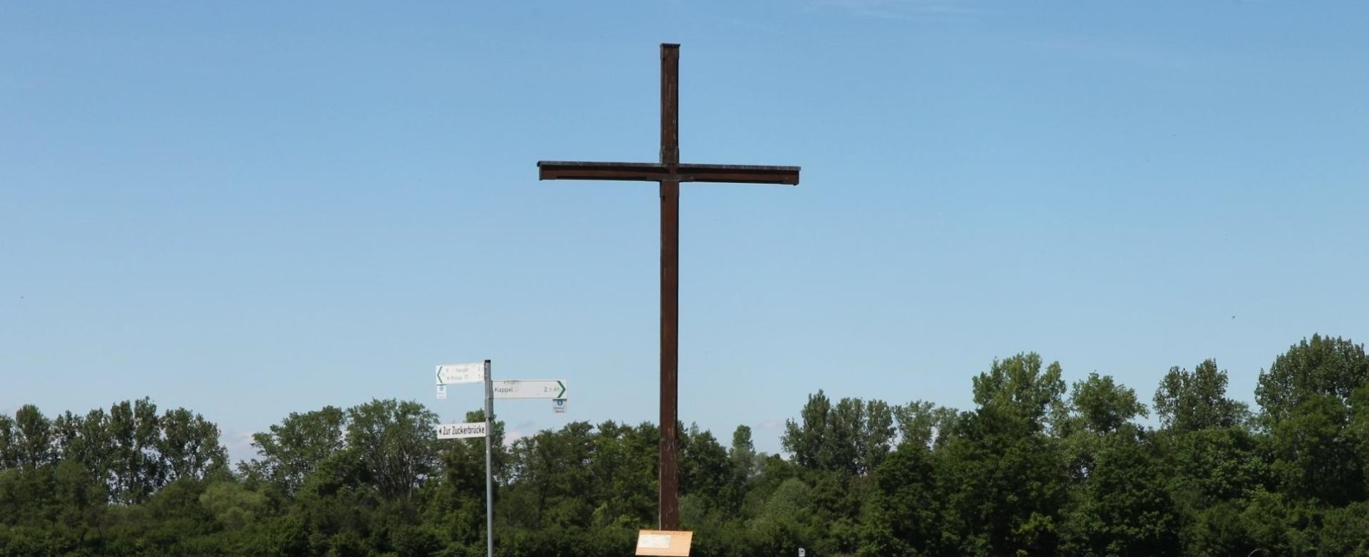 Das Kreuz markiert das Gewann "Amerika" in Rust Ein Weg gabelt sich vor einem großen Holzkreuz, neben dem eine Sitzbank und ein Pfahl mit Schildern stehen.